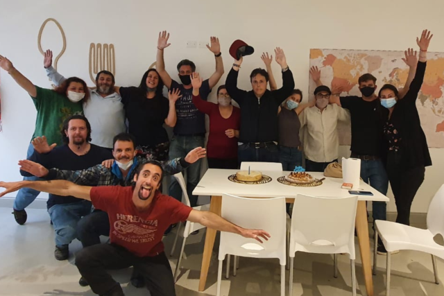 Group of people cheering with arms raised around a table in a bright community room